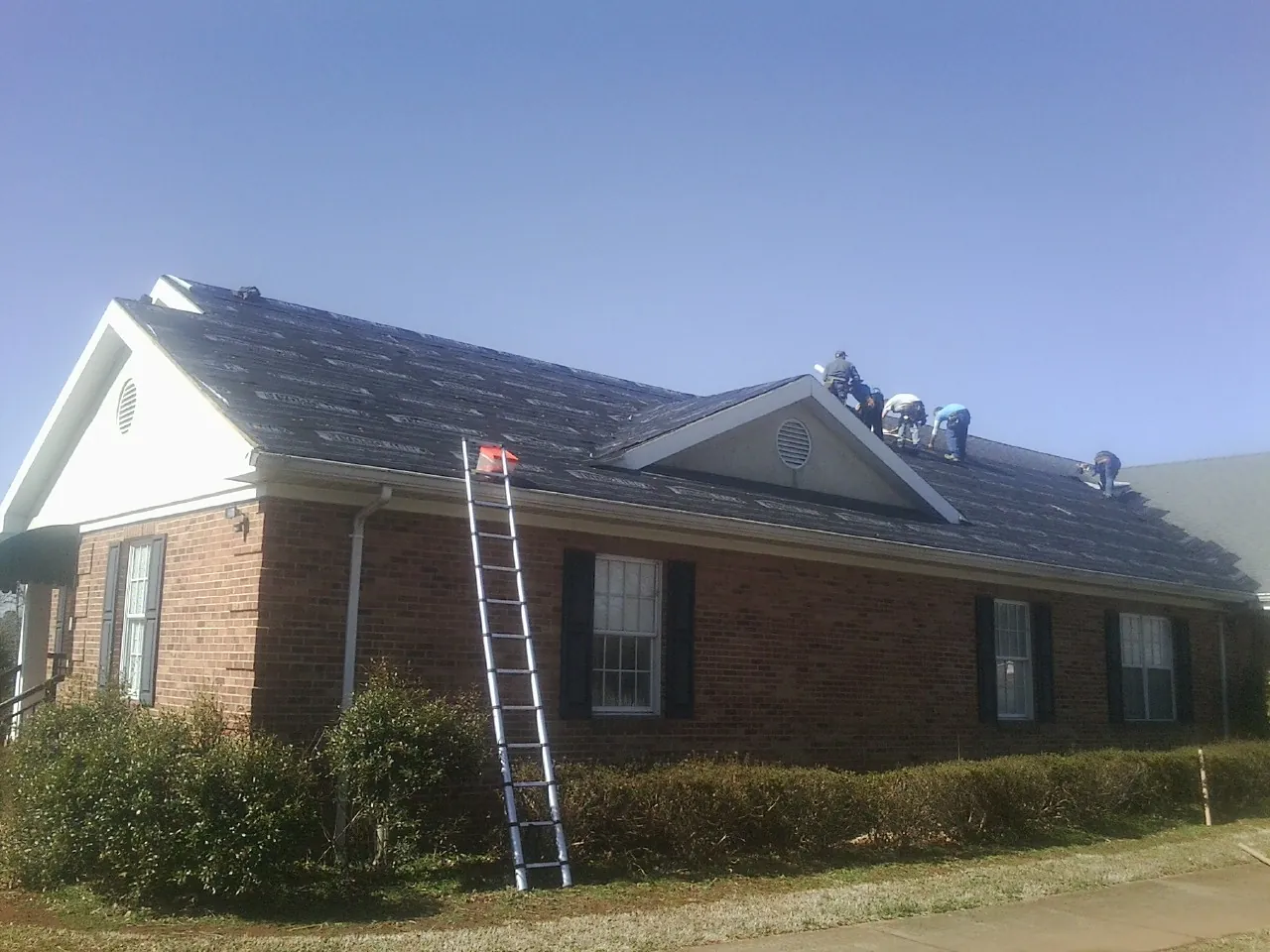 Crew tearing shingles off a brick ranch roof with a ladder set — Metal Roof Repair work by our crew in Tiptonville