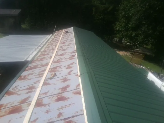 Old rusted panels beside newly installed green metal roofing — Wind Damage Roof Repair by Roofing Brothers in Tiptonville