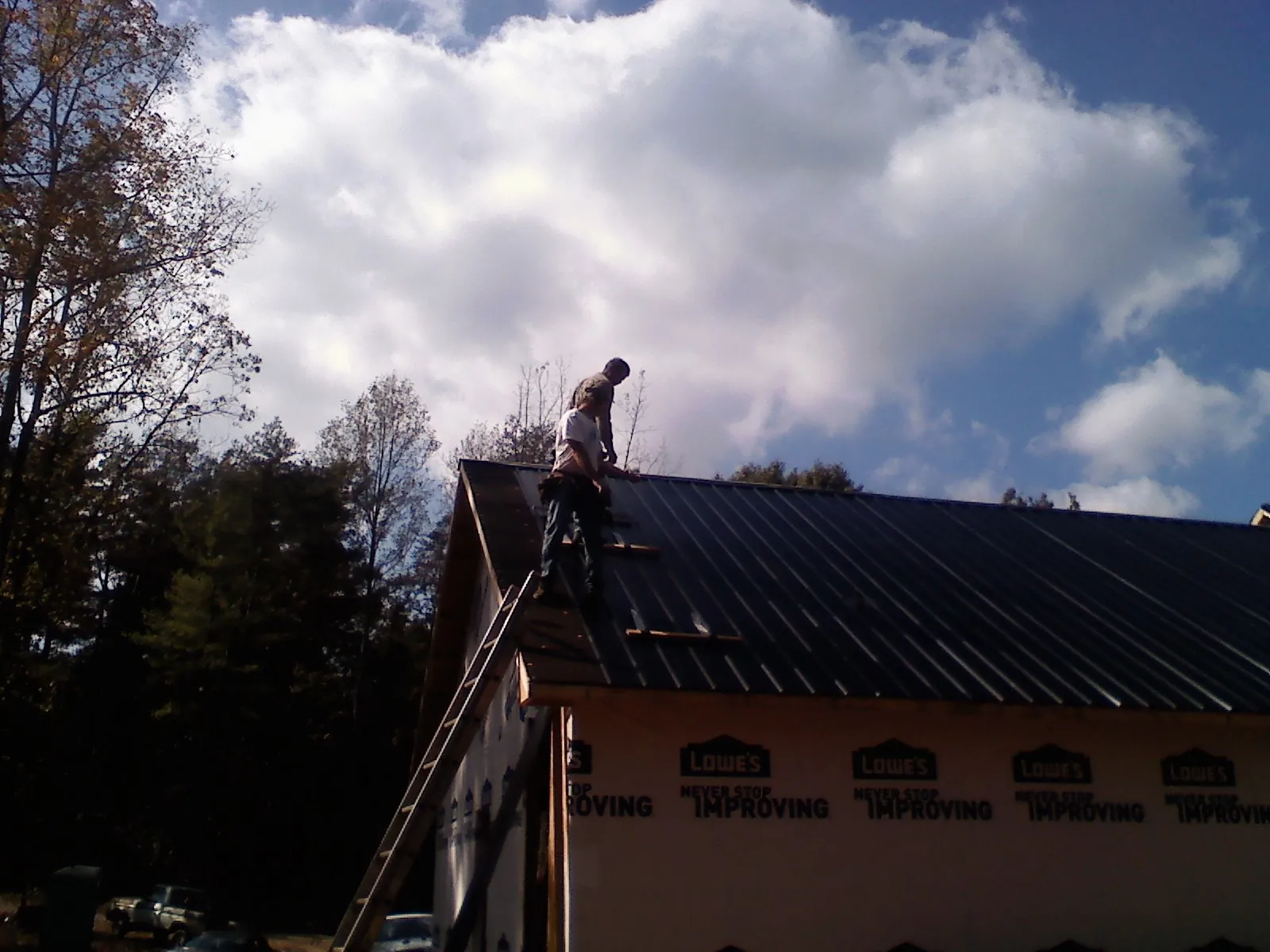 Roofer fastening dark metal panels high against a cloudy sky, from a Roof Inspection job in Tiptonville