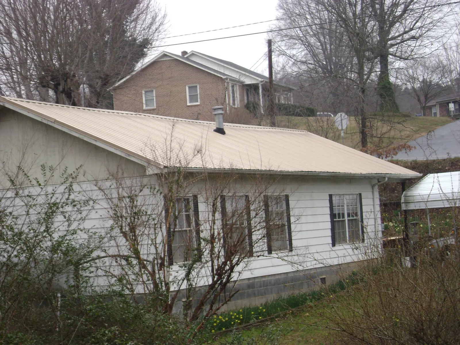 Tan metal roof on a white sided house set into a hillside — Commercial Roofing by Roofing Brothers in Tiptonville